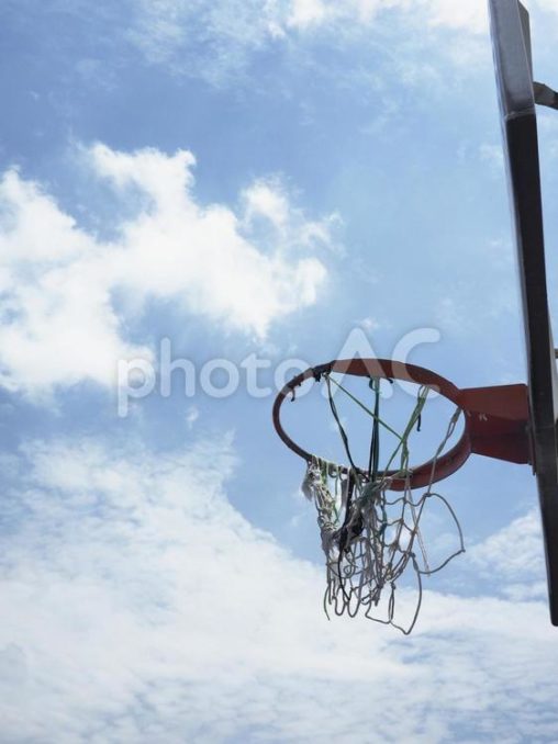 網が破れたバスケットボールリングと青空